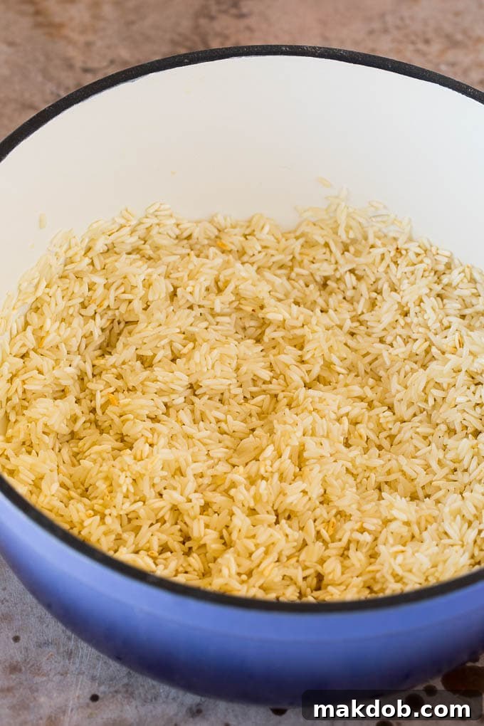 Toasted long-grain white rice shimmering in olive oil within a large pot, showing the golden-brown color achieved before liquid is added.