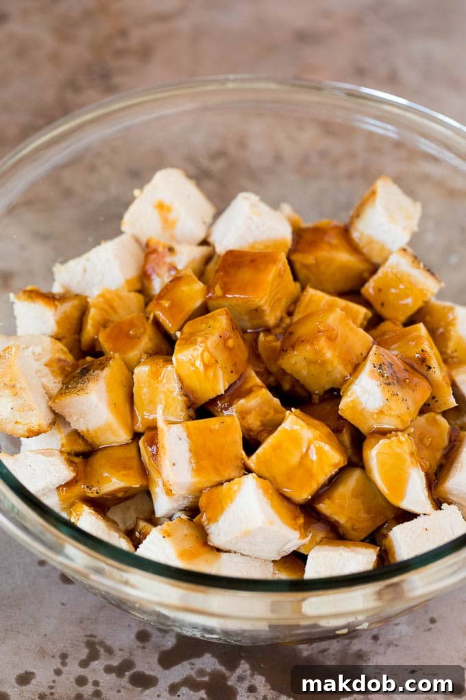 Succulent Teriyaki Chicken Coated in Homemade Sauce Perfectly diced chicken pieces glistening, generously coated in a rich, homemade teriyaki sauce, ready to be incorporated into a delicious bowl.