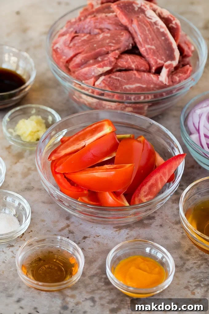Bowls of ingredients including sliced red onions, ripe Roma tomatoes, thinly sliced beef tenderloin, and a selection of seasonings, ready for cooking Lomo Saltado.
