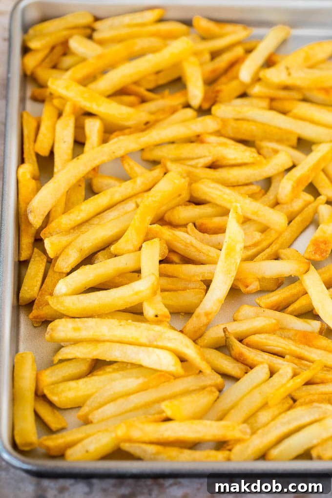 French fries spread evenly on a sheet pan, ready for baking to golden perfection.