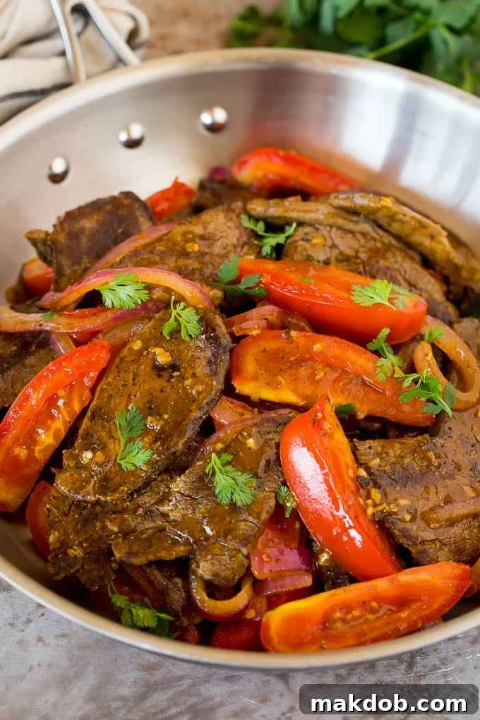 A pan of lomo saltado, showing the stir-fried beef, vibrant tomatoes, onions, and fresh cilantro, with a rich savory sauce.