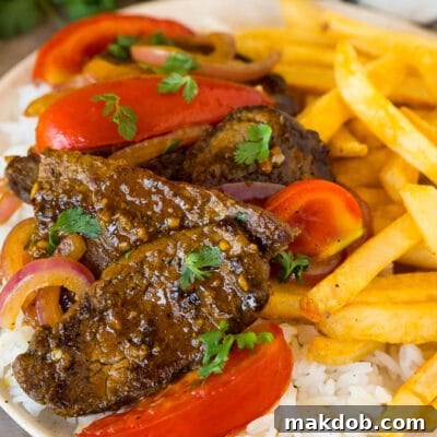 A plate of lomo saltado served with rice and french fries.