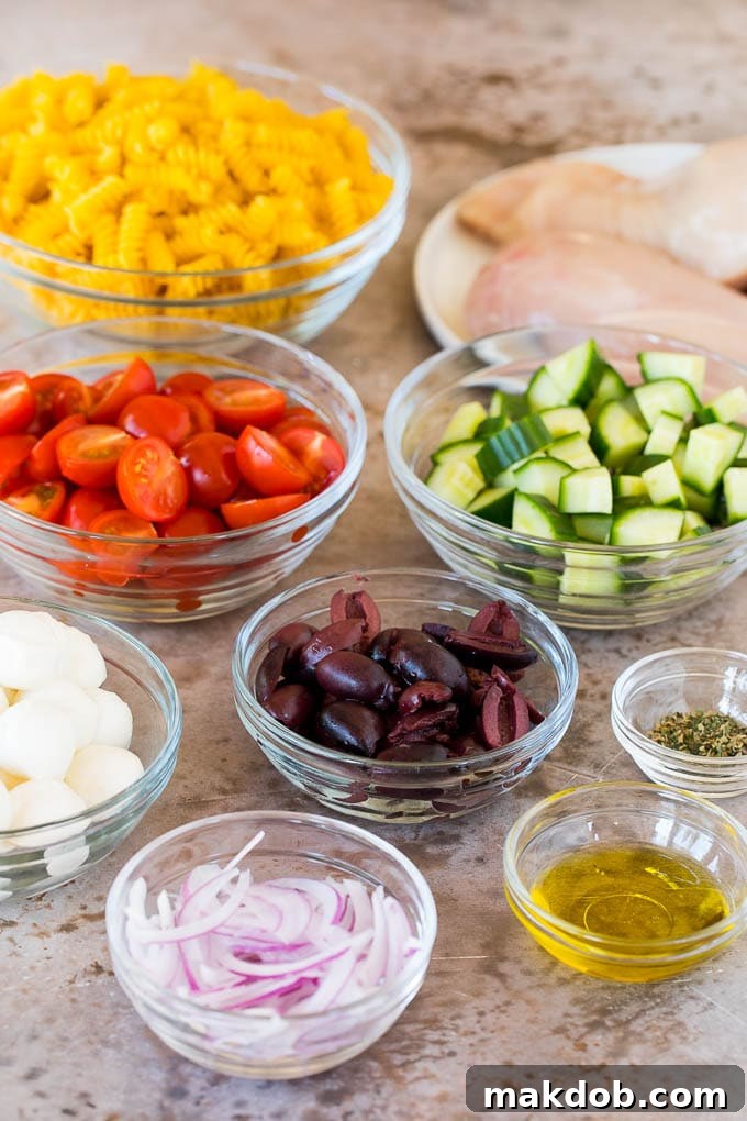 A selection of raw ingredients for chicken pasta salad, including dry rotini pasta, fresh cucumber, cherry tomatoes, and kalamata olives, ready for preparation.