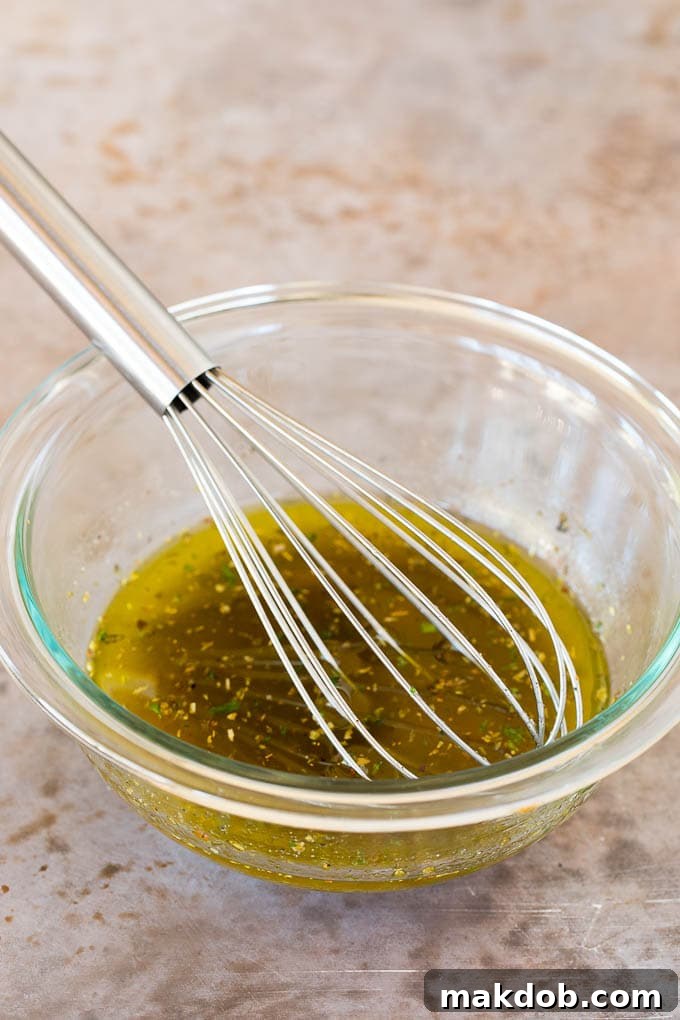 A bowl of freshly made homemade Italian dressing with a whisk, showcasing the vibrant colors of olive oil, herbs, and spices.