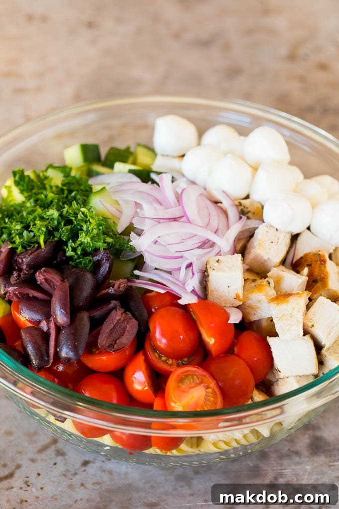 A close-up shot of grilled chicken, vibrant vegetables, and briny olives mingling beautifully with al dente pasta in a large serving bowl, awaiting the final dressing.