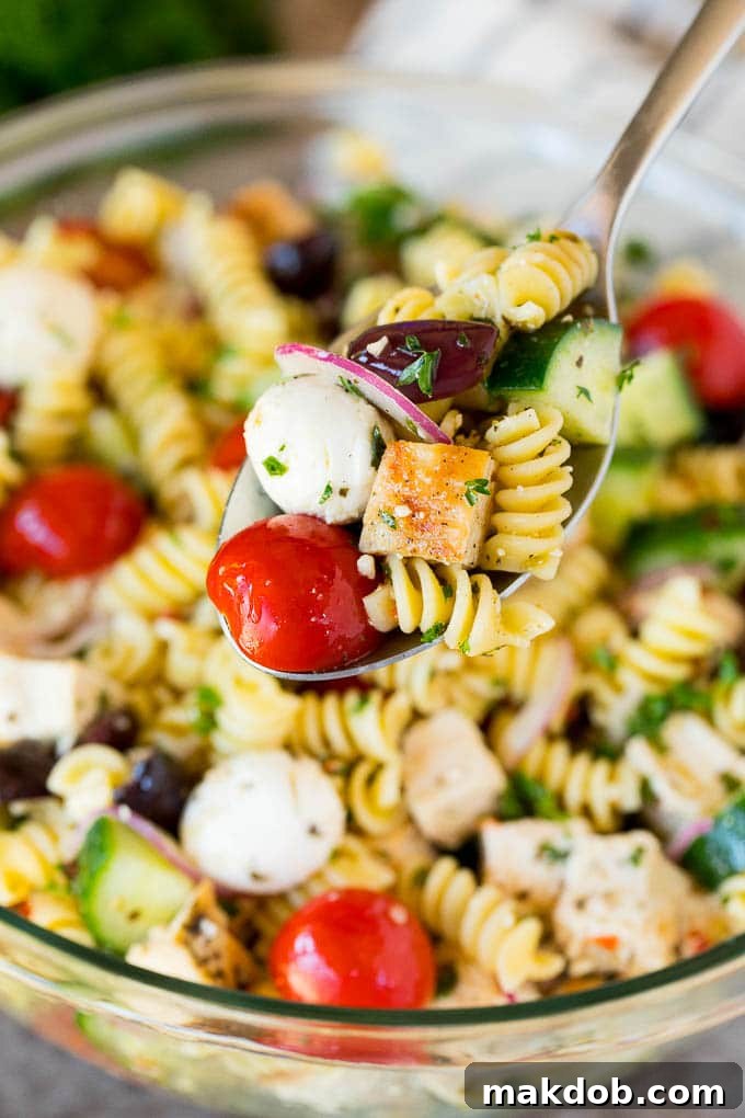 A serving spoon lifting a portion of chicken pasta salad, showcasing its rich texture and colorful ingredients.