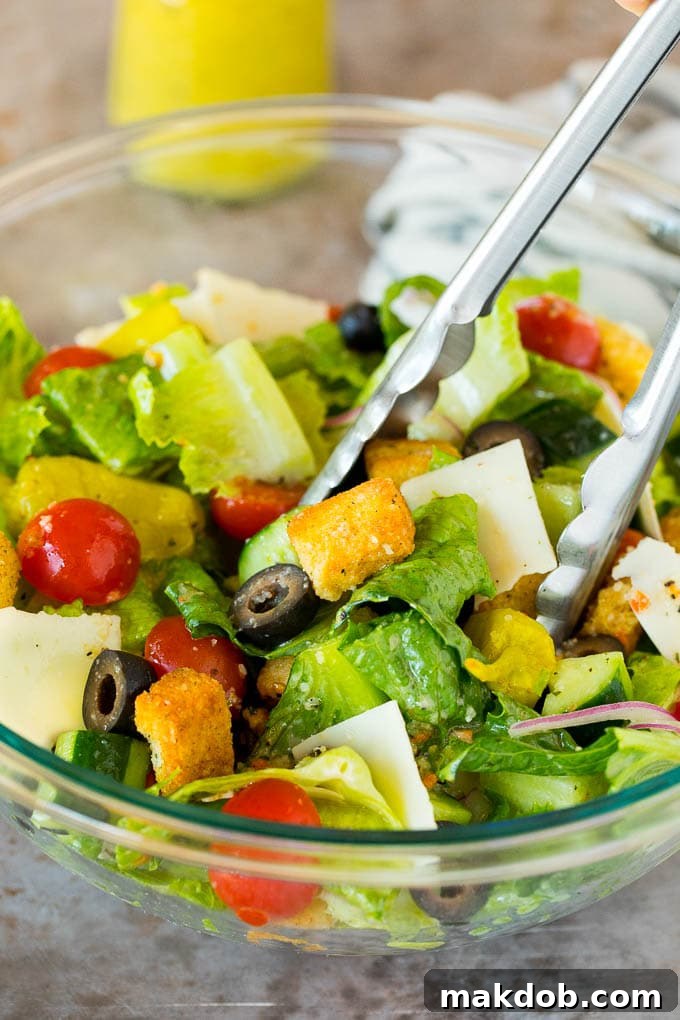 Serving Italian Salad Tongs gently serving a portion of fresh Italian salad from a large bowl, highlighting the crisp greens, tomatoes, olives, and cheese.