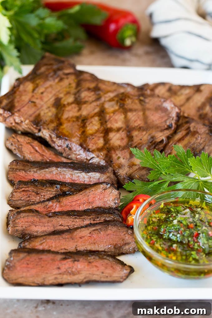Sliced churrasco served with a bowl of chimichurri sauce, garnished with fresh herbs.