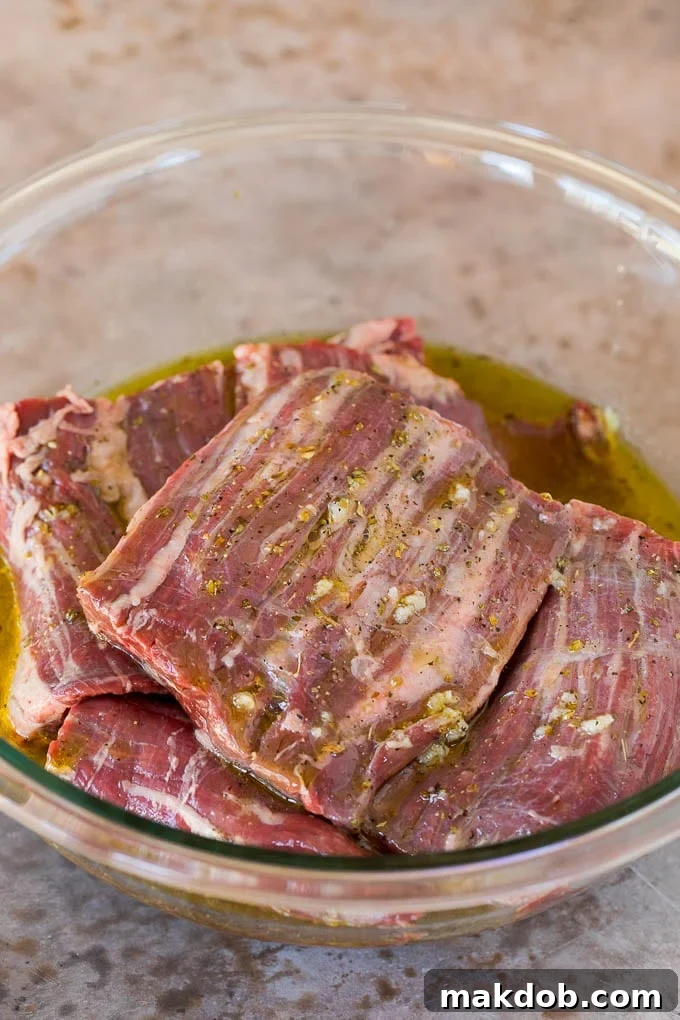 Skirt steak generously coated in a flavorful olive oil and citrus marinade in a bowl.