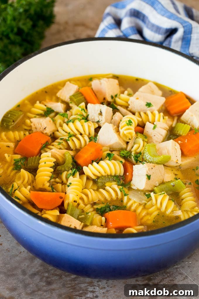 A pot of homemade turkey noodle soup with chunks of turkey, vegetables, and pasta, garnished with fresh parsley.
