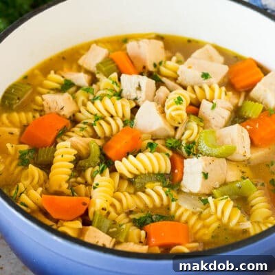 A pot of homemade turkey noodle soup with vegetables, garnished with parsley.