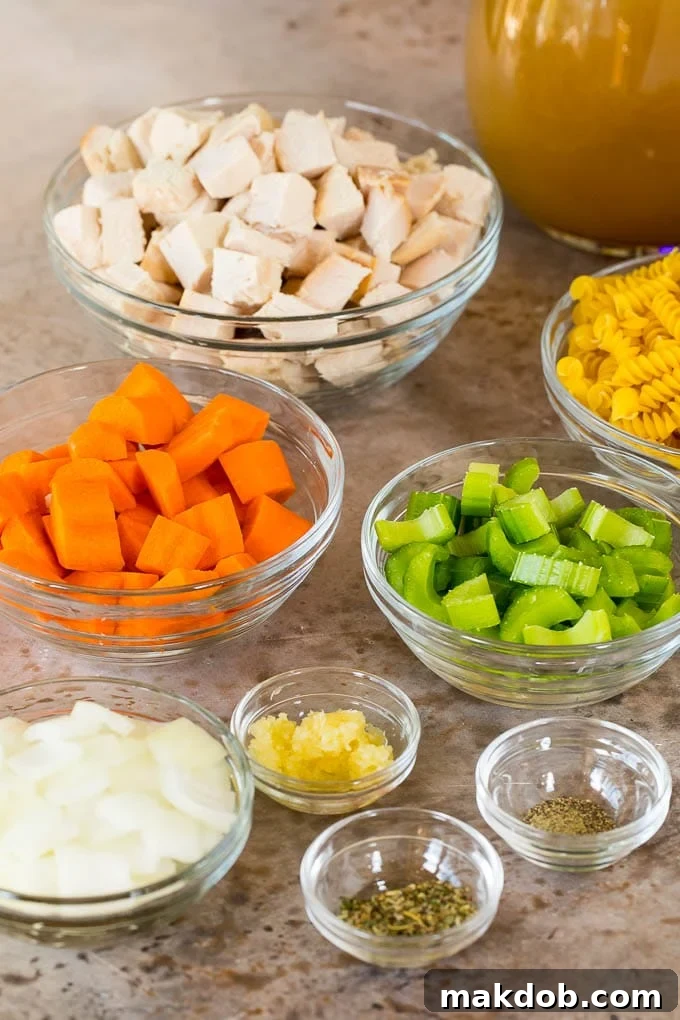 Bowls filled with diced turkey, chopped vegetables, and uncooked pasta, ready to be added to the soup.