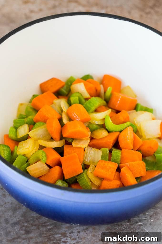 Sautéed carrots, onions, and celery glistening in butter in a large pot, the aromatic base for the soup.