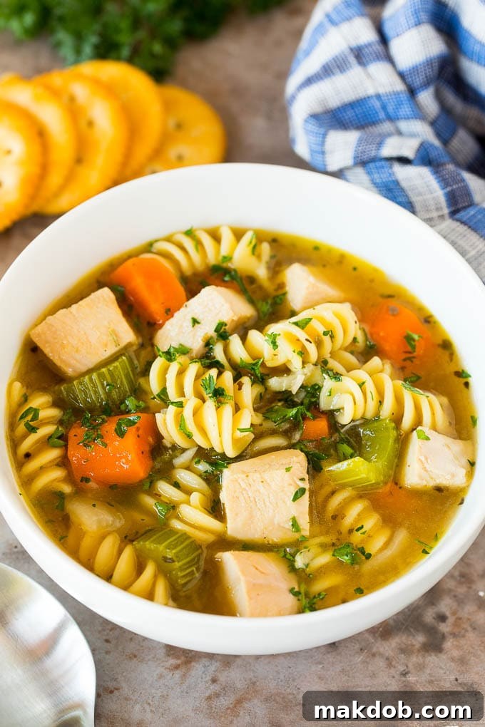 A steaming bowl of turkey noodle soup, garnished with fresh parsley and served with a side of crackers.
