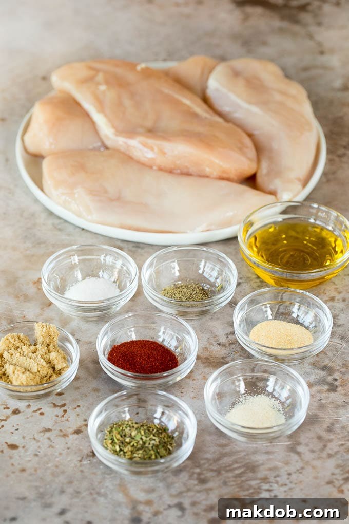 This air fryer chicken breast recipe consists of chicken coated in herbs and spices, then cooked to golden brown perfection. Chicken on a plate with bowls of herbs and spices.