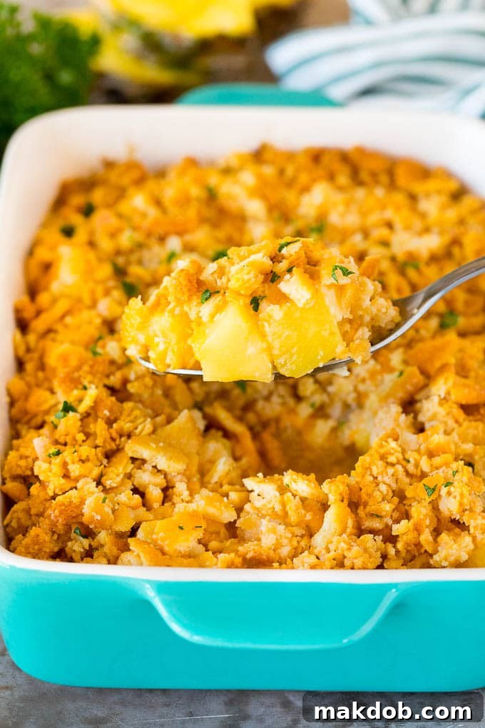 A spoon holding a serving of pineapple casserole topped with crackers and parsley.