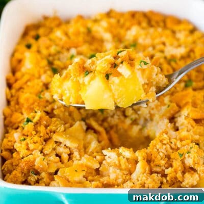 A spoon holding a serving of pineapple casserole topped with crackers and parsley.