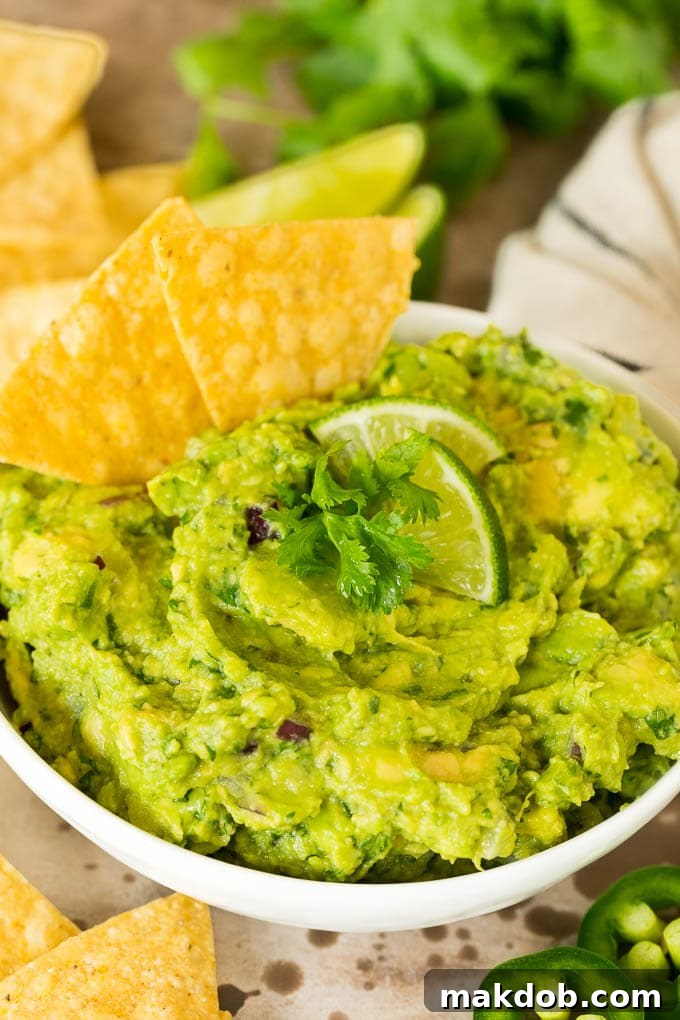 Copycat Chipotle Guacamole 2 A vibrant bowl of homemade Chipotle guacamole, perfectly mashed and topped with fresh cilantro, served with a generous pile of crispy tortilla chips ready for dipping. The setting evokes a cozy home kitchen, promising delicious, restaurant-quality flavor.
