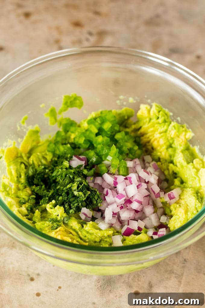 Copycat Chipotle Guacamole 4 A bowl of freshly mashed avocado being mixed together with finely diced red onion, vibrant chopped cilantro, and a hint of jalapeño, showcasing the vibrant and fresh ingredients essential for homemade Chipotle guacamole.