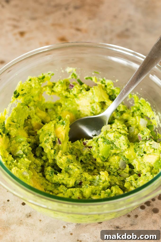 Copycat Chipotle Guacamole 5 A beautifully textured bowl of homemade guacamole, showcasing the perfectly blended avocados with visible, finely diced bits of red onion, vibrant cilantro, and a hint of jalapeño, all artfully arranged and ready to be enjoyed as a dip.