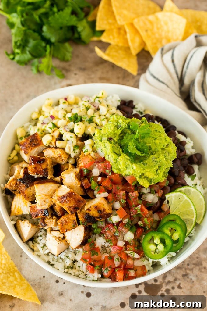 Copycat Chipotle Guacamole 6 A vibrant and appetizing burrito bowl, generously topped with savory grilled chicken, fluffy rice, seasoned black beans, fresh chunky salsa, and a large, inviting dollop of creamy homemade Chipotle guacamole, perfectly prepared for a delicious and satisfying meal.