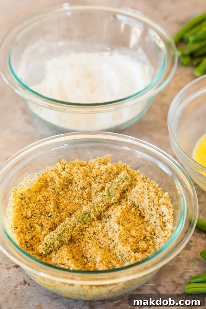 A green bean dipped in a bowl of seasoned breadcrumbs.