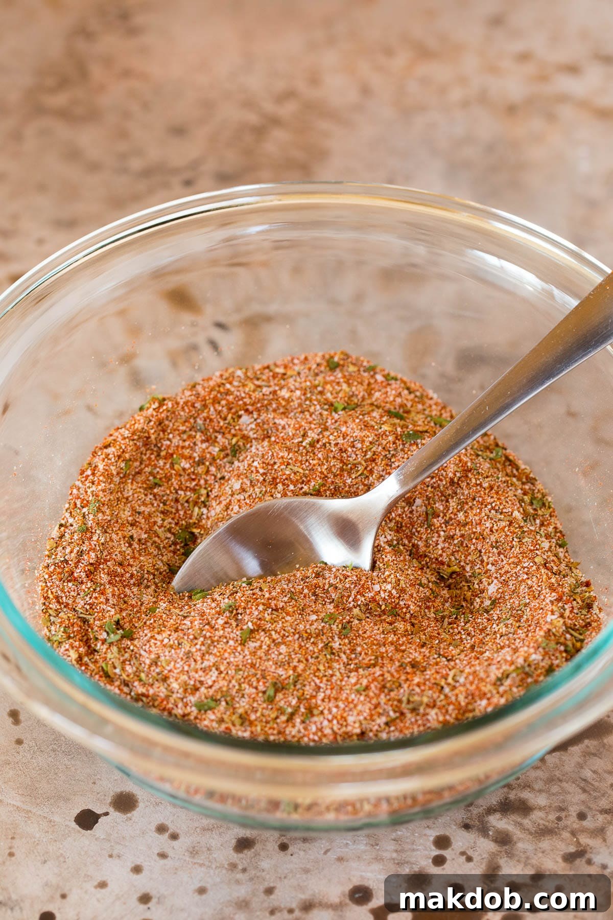 A bowl of homemade Creole seasoning with a spoon, ready to be used in various dishes.