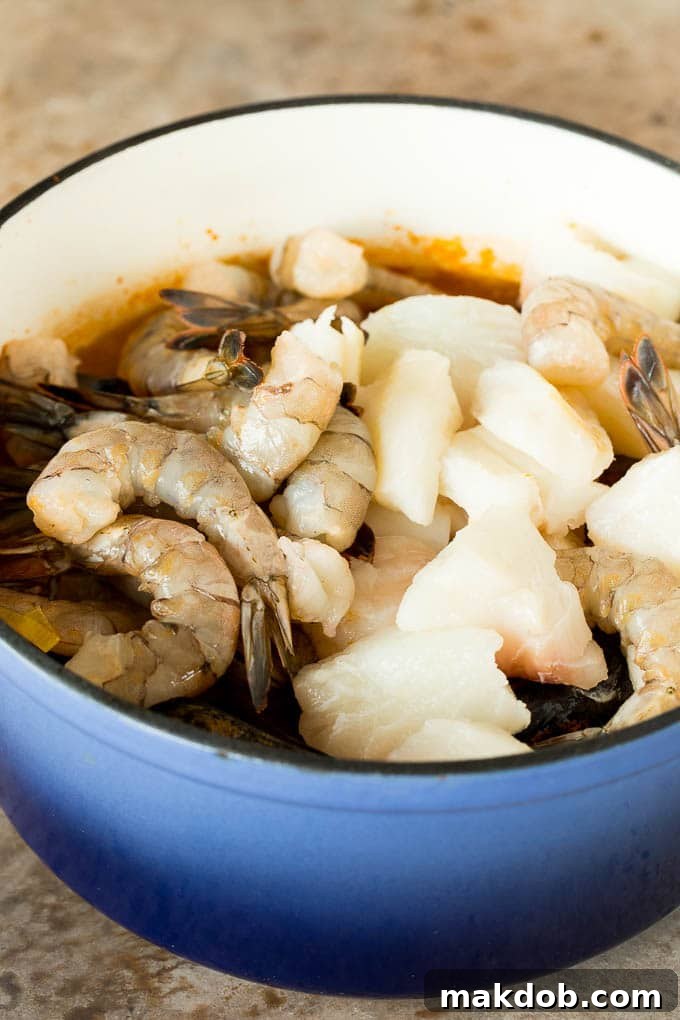 This bouillabaisse is French seafood stew with fresh fish, shrimp, clams and mussels, all simmered together in a flavorful broth. A pot with broth, fish and shrimp in it.