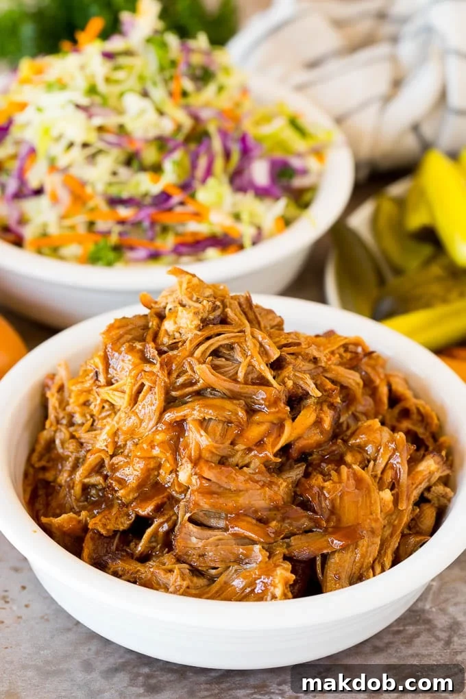 A bowl of Instant Pot pulled pork served with a side of creamy coleslaw and crunchy pickles, perfect for a balanced meal.