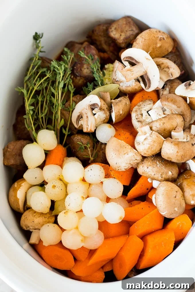 This slow cooker beef bourguignon is tender beef chunks, bacon, mushrooms, carrots and pearl onions, all simmered together in a rich red wine broth. A slow cooker filled with vegetables, browned beef and herbs.