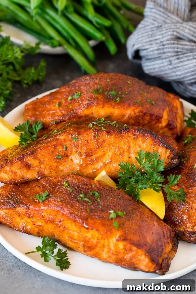 This air fryer salmon is fresh fish fillets topped with a homemade spice rub, then cooked to golden brown perfection. A plate of air fryer salmon fillets garnished with lemon and herbs.