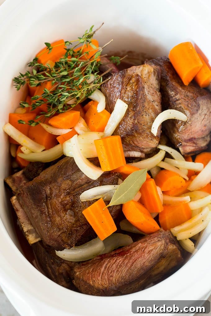Fall-Off-The-Bone Slow Cooker Short Ribs 5 Short ribs in a slow cooker with sauce, carrots and herbs.