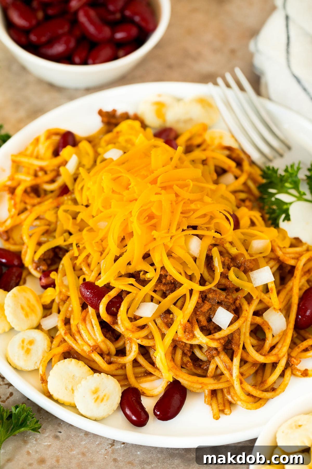 A meticulously arranged plate of spaghetti topped with Cincinnati chili, accompanied by sides of kidney beans, oyster crackers, and shredded cheese for a complete meal.