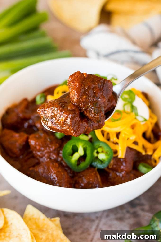 A spoon lifting a hearty serving of dark, rich Texas chili, showcasing its thick consistency and tender meat chunks.