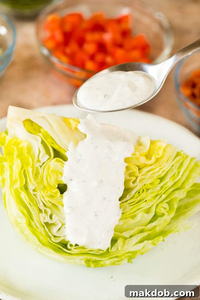Crisp Wedge Salad with Blue Cheese 5 A spoon pouring dressing over a wedge of lettuce.
