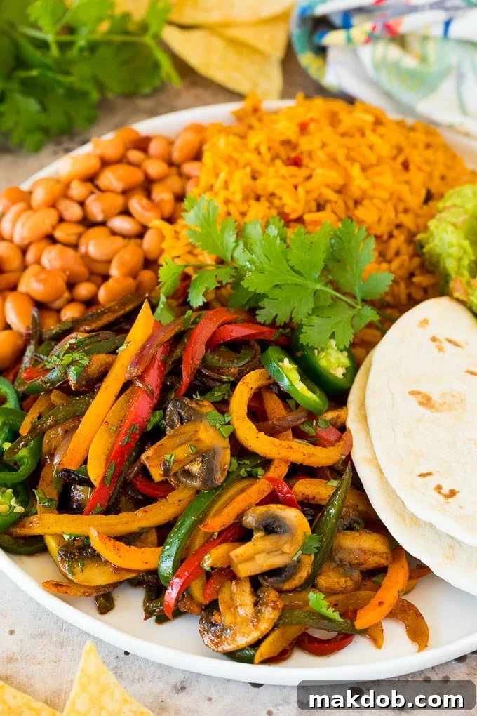 A vibrant platter of freshly cooked vegetarian fajitas, featuring an assortment of colorful peppers, sliced red onions, and browned mushrooms. The fajitas are garnished with fresh cilantro and served alongside fluffy rice and black beans, ready to be wrapped in warm tortillas.
