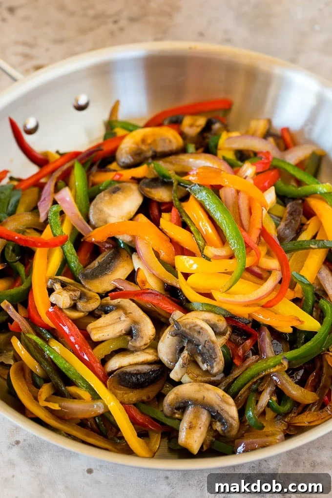 A close-up shot of a pan filled with beautifully cooked peppers and mushrooms for vegetarian fajitas, showing the perfect char and tender texture.