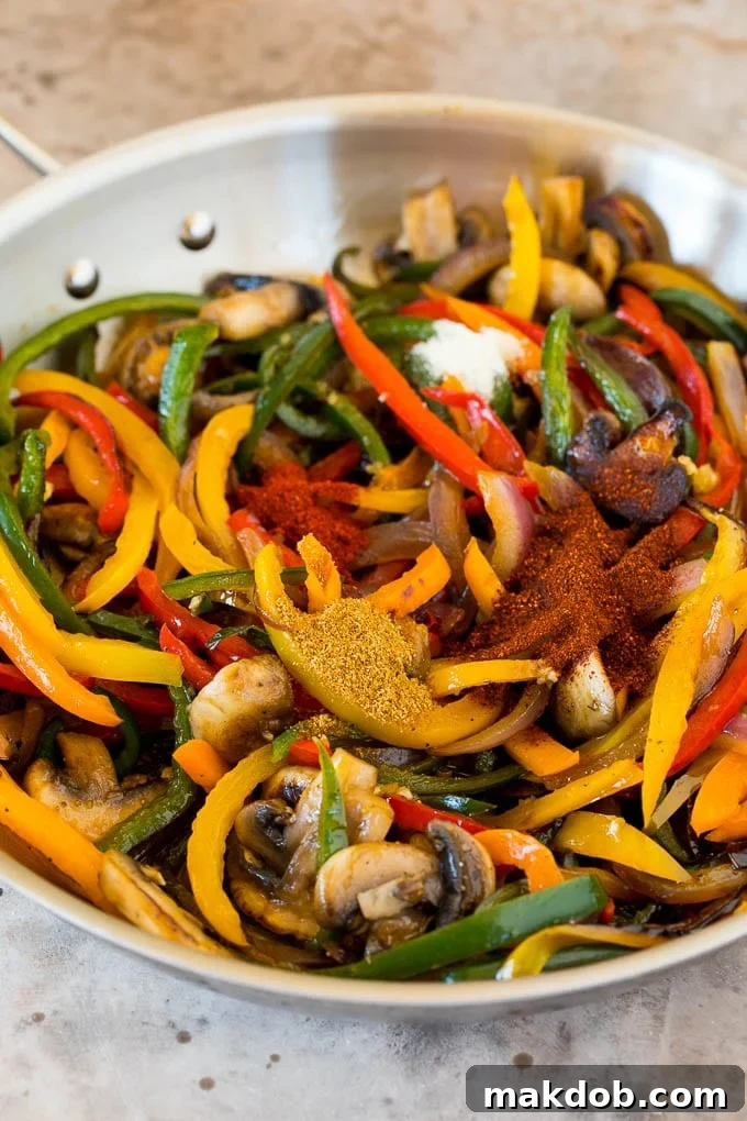 A pan of sautéed red onions and colorful bell peppers, lightly seasoned with spices, illustrating the initial cooking phase of vegetarian fajitas.