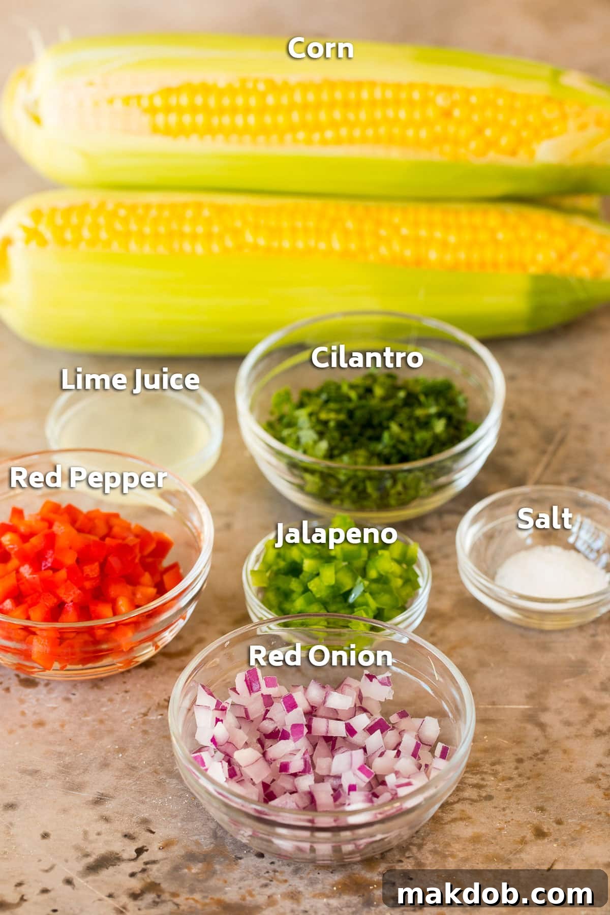 Fresh ingredients including corn on the cob, bright red bell peppers, red onion, cilantro, and jalapeno, ready for corn salsa.