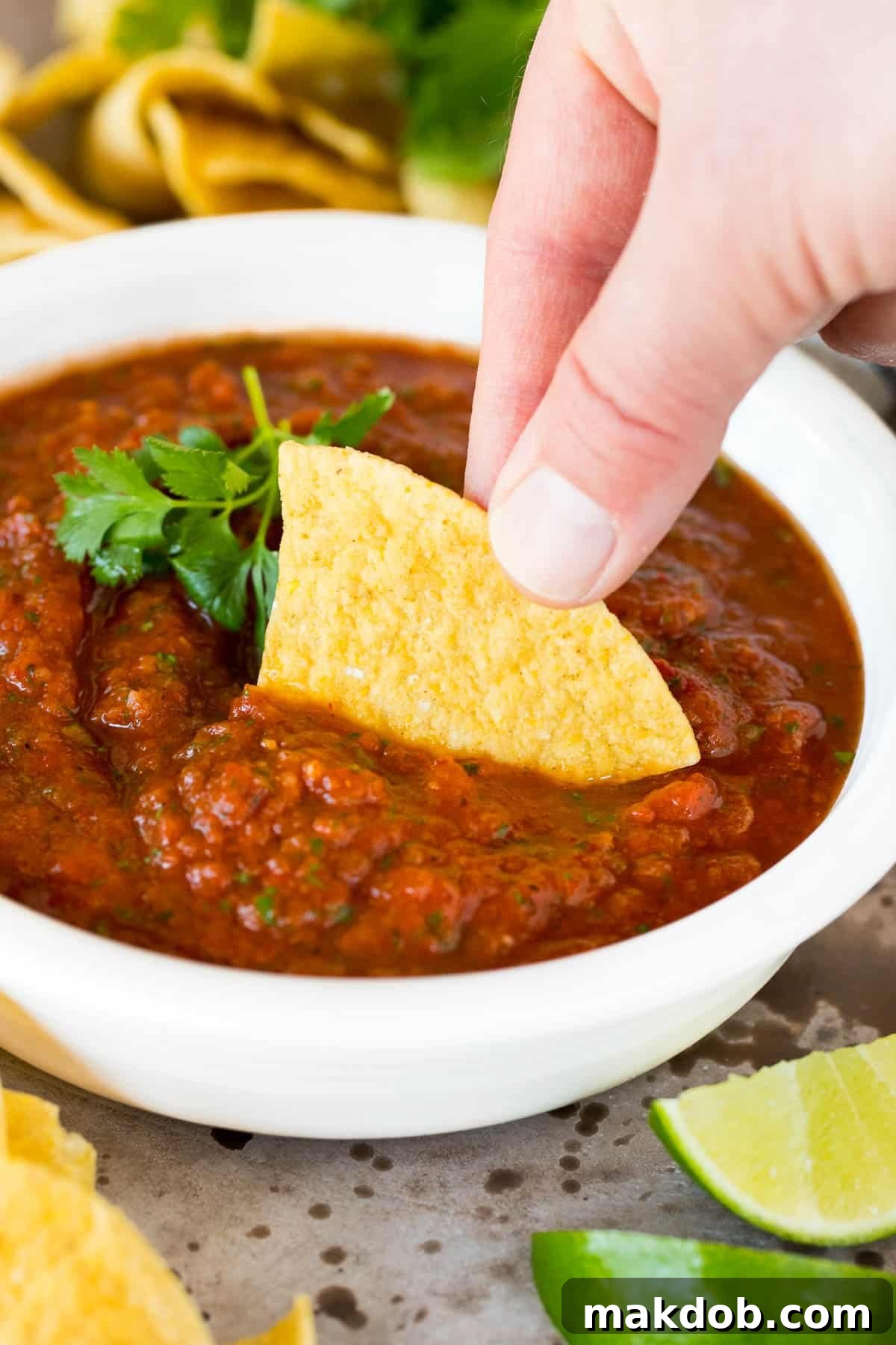 A crispy tortilla chip scooping up a generous portion of homemade tomato chipotle salsa, highlighting its inviting texture and vibrant color.