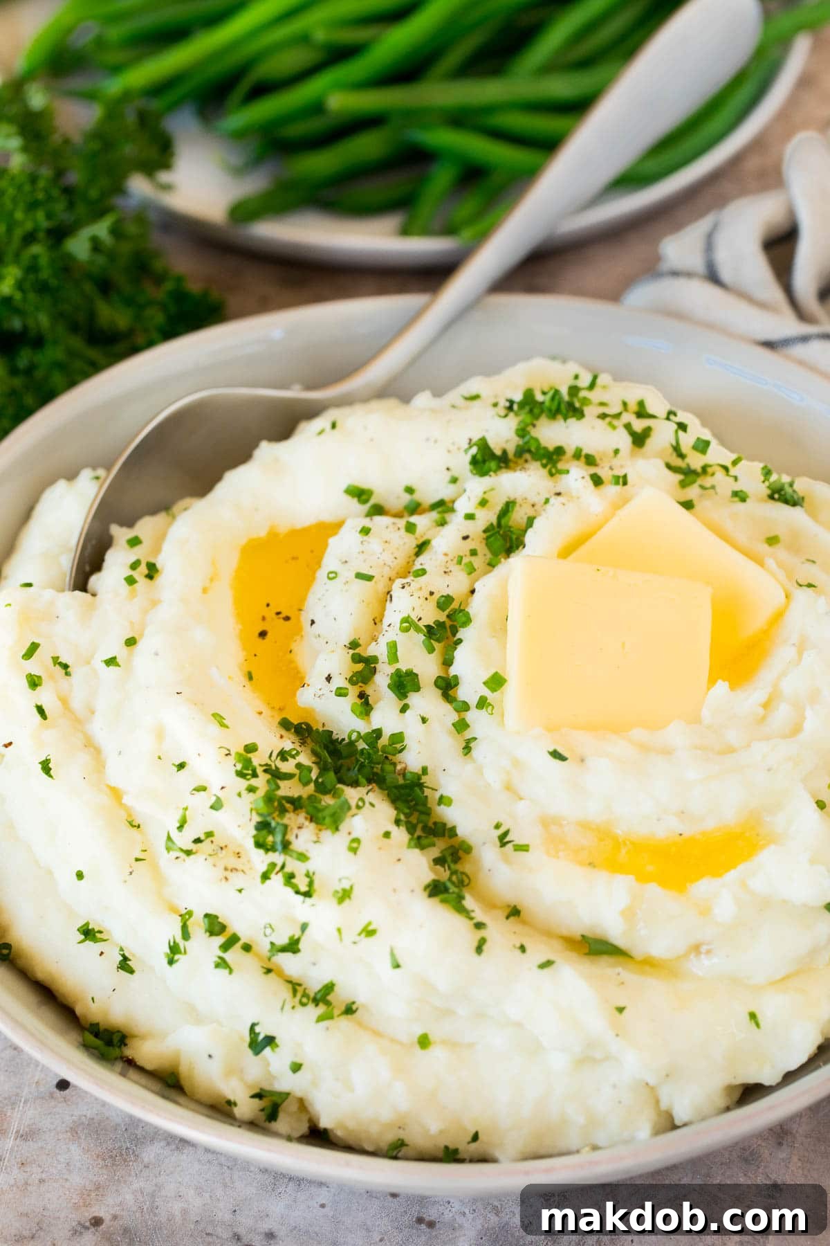 These make ahead mashed potatoes are Russet potatoes that are boiled until tender, then combined with butter, garlic, cream cheese and seasonings to make the ultimate side dish. A bowl of make ahead mashed potatoes topped with butter and fresh herbs, ready to be served for a holiday feast.