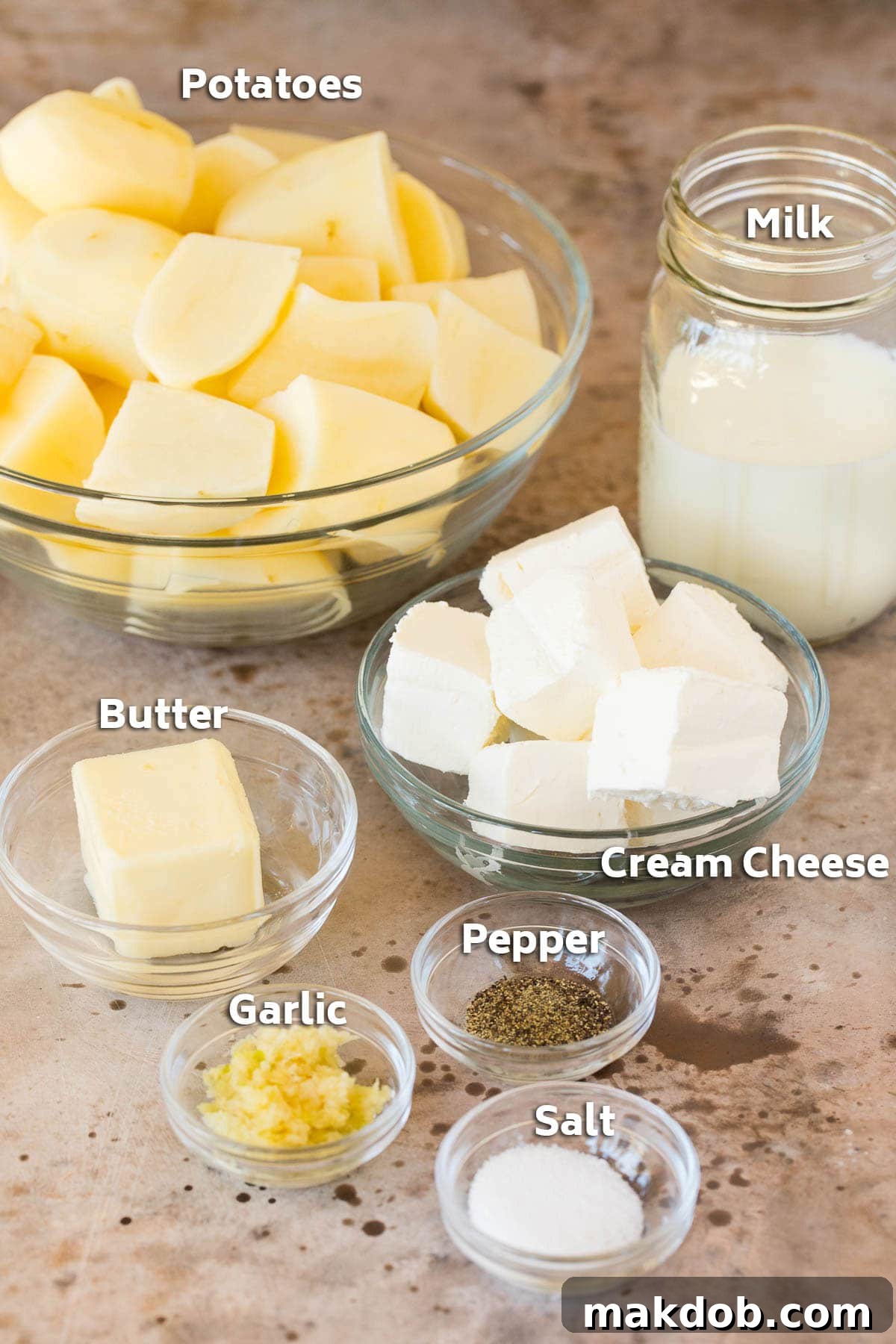 Cook-Ahead Creamy Mash 2 Bowls showcasing the key ingredients for make ahead mashed potatoes: whole potatoes, cream cheese, butter, and seasonings.