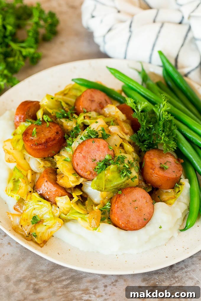 This cabbage and sausage skillet is a combination of smoked sausage, vegetables and savory seasonings, all cooked together to make a quick and easy dinner. A plate of cabbage and sausage served over mashed potatoes with green beans.