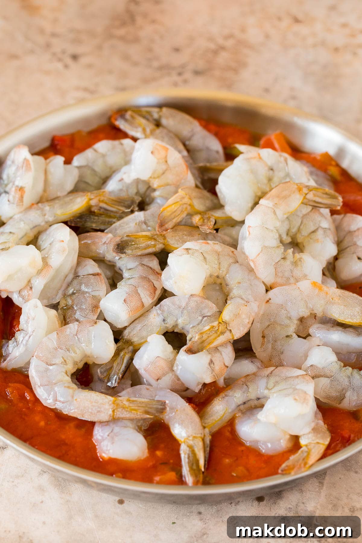 Raw shrimp in a pan of tomato sauce.