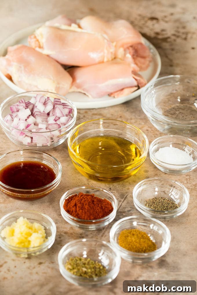Chicken thighs with bowls of spices, olive oil, onion and garlic.