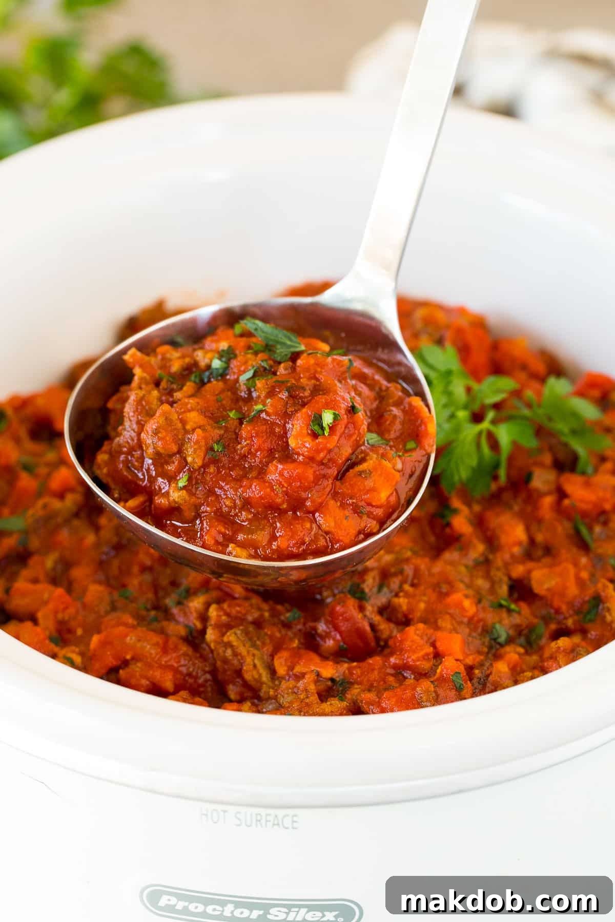A ladle lifts a generous serving of rich, red slow cooker bolognese sauce, showing its thick texture.