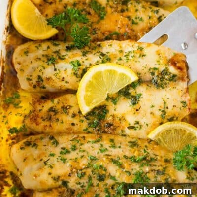 A spatula serving baked tilapia garnished with herbs and lemon.