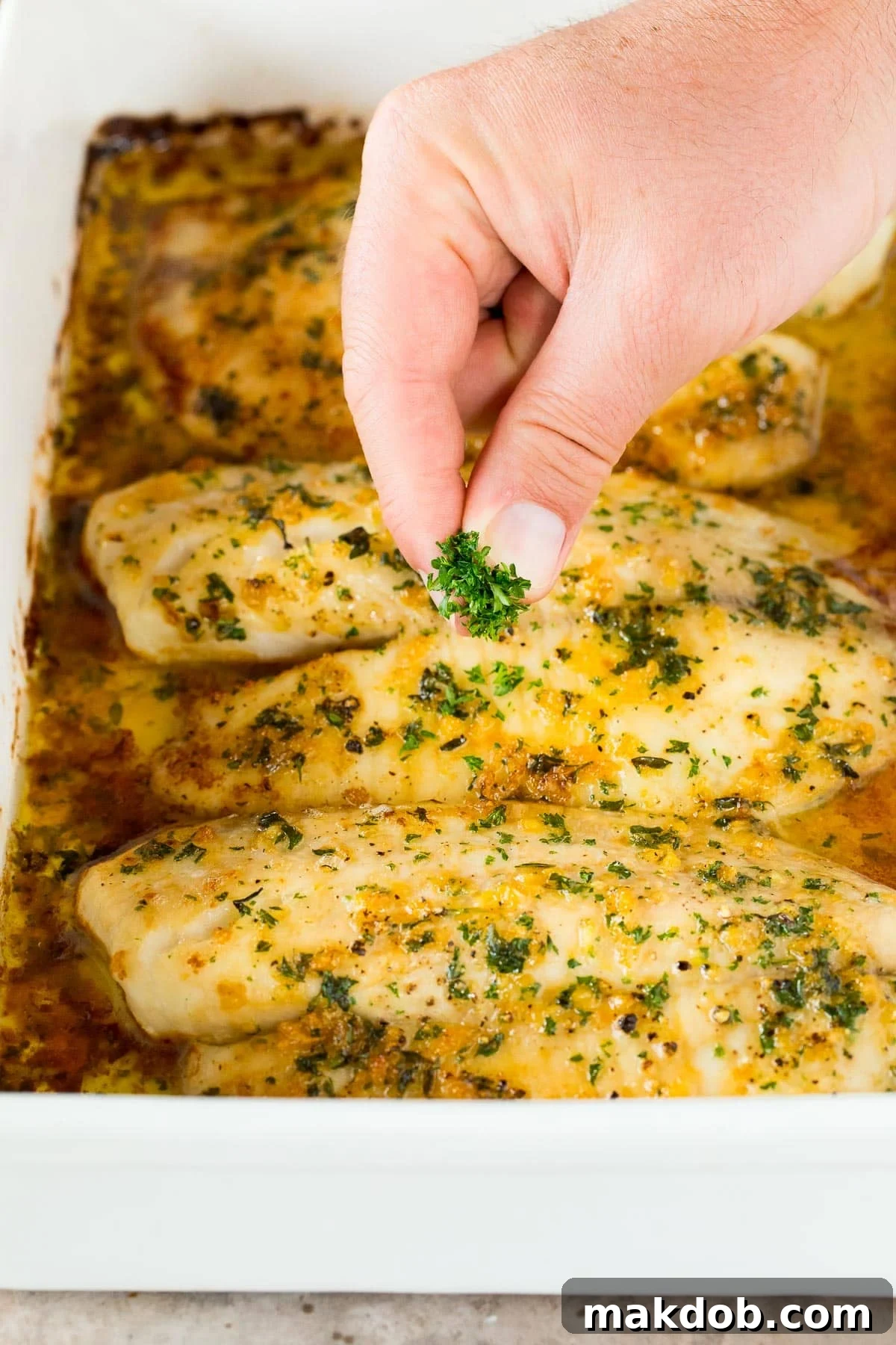 Savory Garlic Butter Tilapia Bake 5 A hand sprinkling parsley over fish.