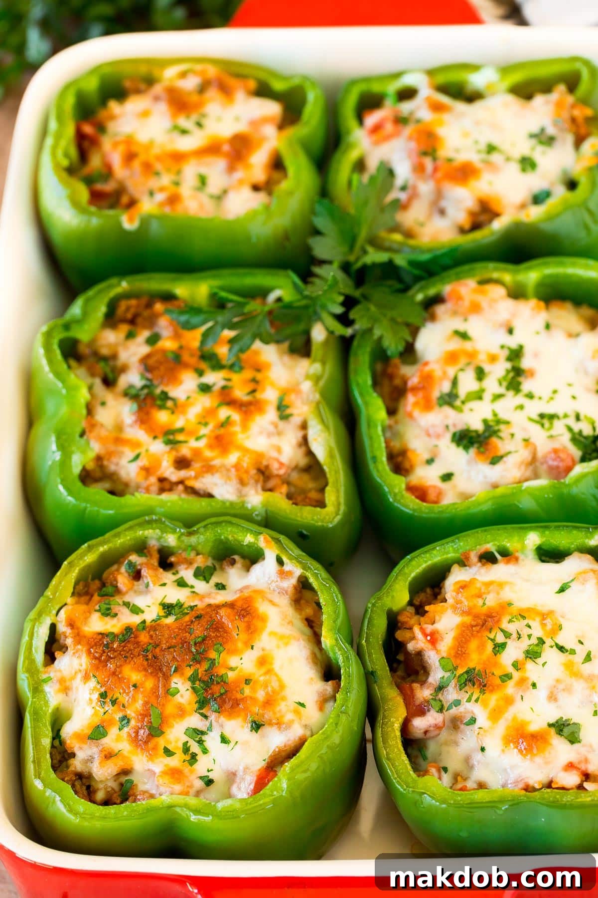 Stuffed green peppers topped with a generous layer of melted cheese, baked golden brown in a white baking dish.