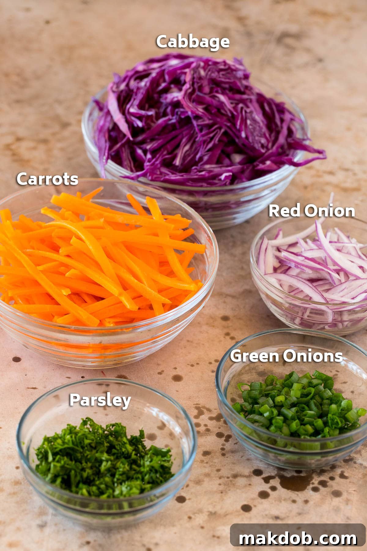 Bowls of shredded red cabbage, carrots, red onions, and chopped parsley and green onions.